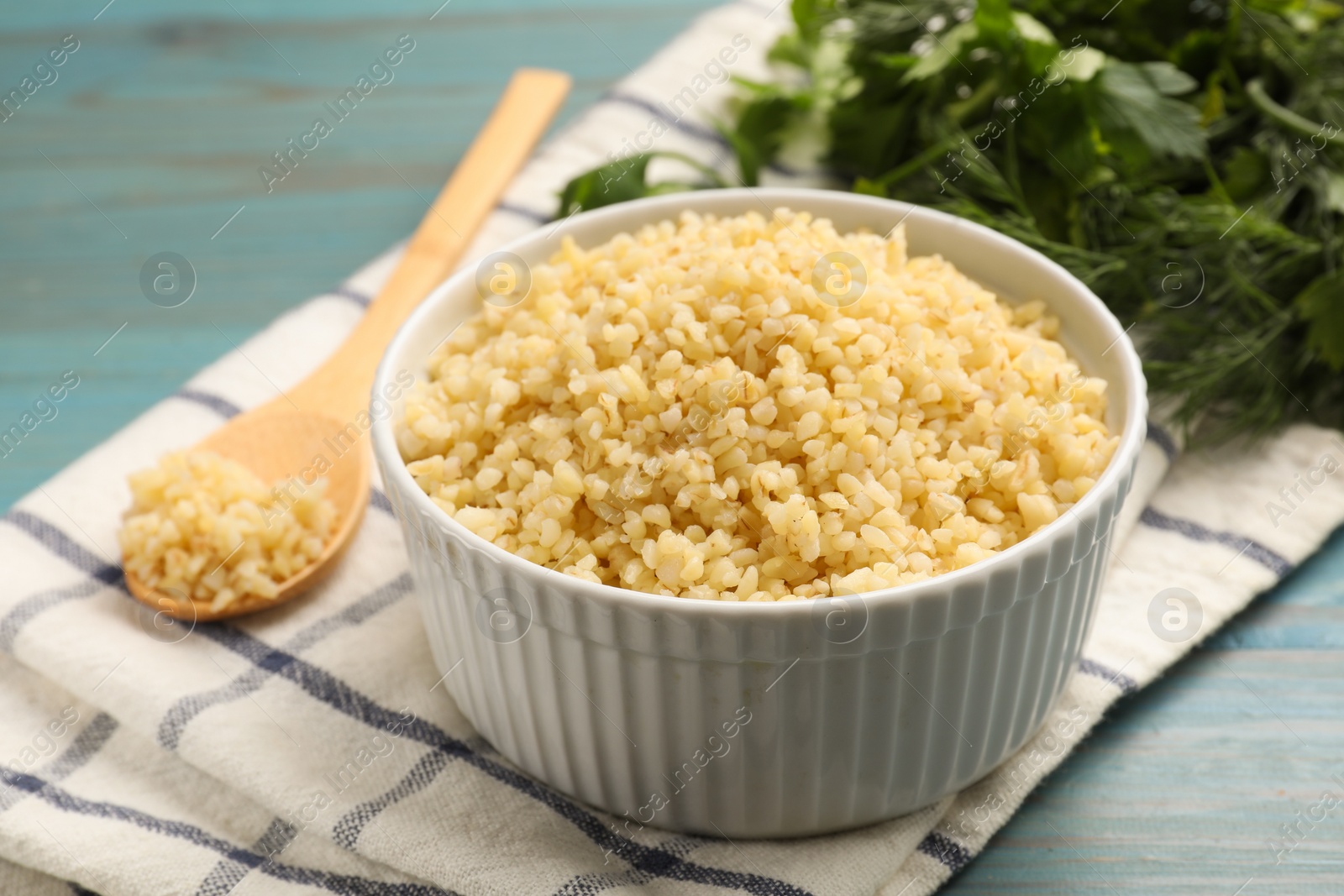 Photo of Delicious bulgur in bowl on light blue wooden table, closeup