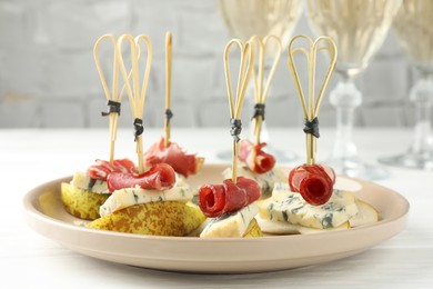 Photo of Tasty canapes with pears, blue cheese and prosciutto on white wooden table, closeup