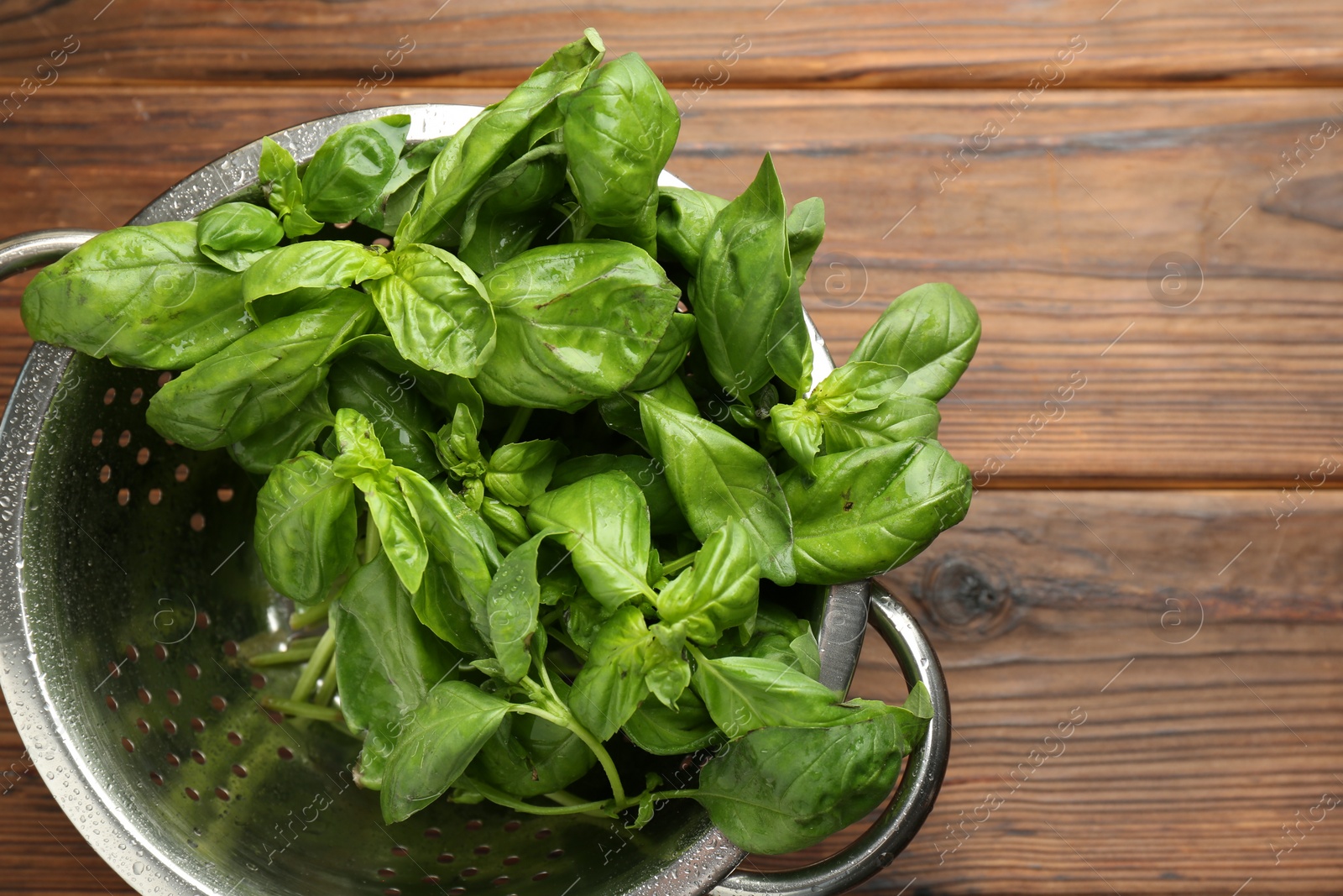 Photo of Metal colander with fresh basil leaves on wooden table, top view. Space for text