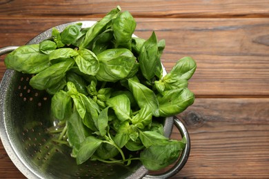 Metal colander with fresh basil leaves on wooden table, top view. Space for text