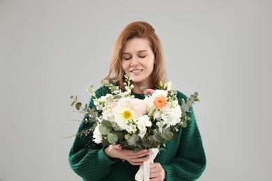 Beautiful woman with bouquet of flowers on grey background