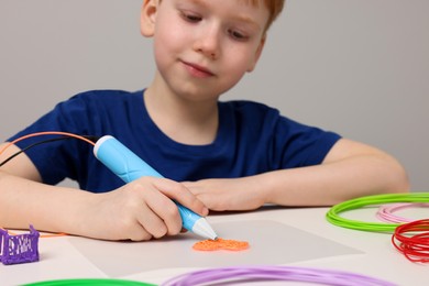 Photo of Boy drawing with stylish 3D pen at white table, selective focus