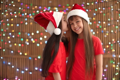 Photo of Cute little children in Santa hats on blurred lights background. Christmas celebration