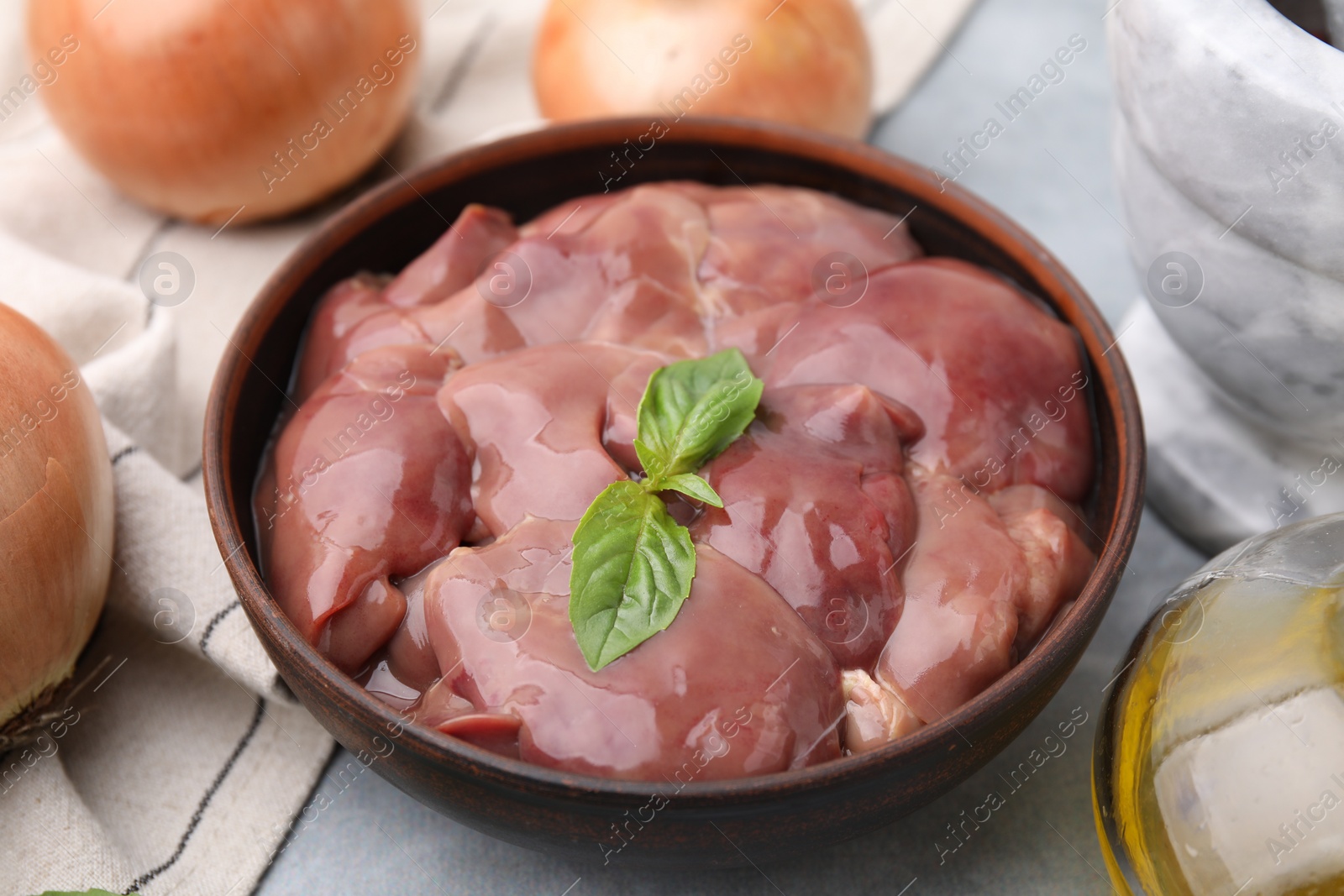 Photo of Bowl with raw chicken liver and basil on light grey table, closeup