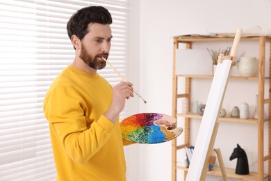 Photo of Man painting in studio. Using easel to hold canvas