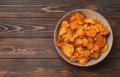 Photo of Plate of sweet potato chips on wooden table, top view. Space for text