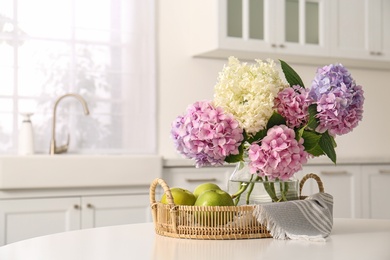 Bouquet of beautiful hydrangea flowers and apples on table in kitchen, space for text. Interior design