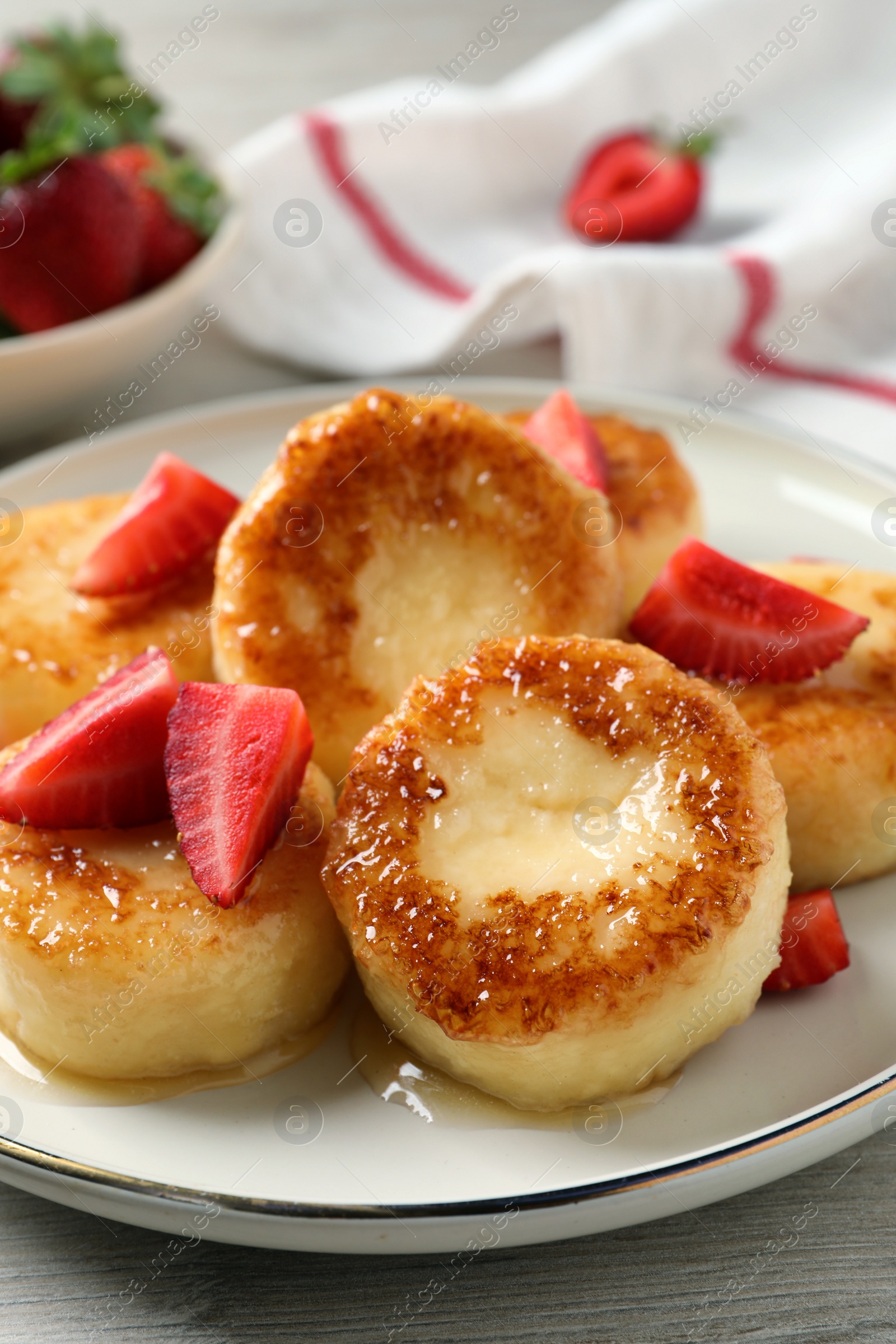 Photo of Delicious cottage cheese pancakes with strawberries and honey on white wooden table, closeup