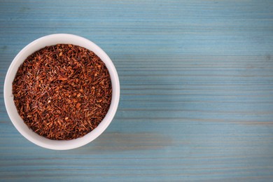 Photo of Dry rooibos leaves in bowl on turquoise wooden table, top view. Space for text