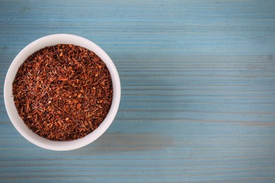 Dry rooibos leaves in bowl on turquoise wooden table, top view. Space for text