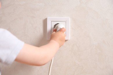 Little child playing with electrical socket and plug indoors, closeup. Dangerous situation