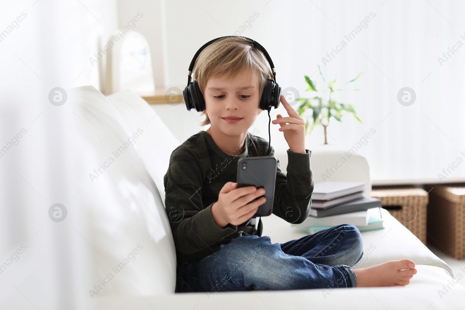 Photo of Cute little boy with headphones and smartphone listening to audiobook at home