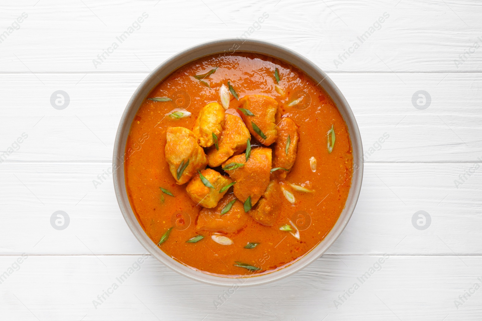 Photo of Bowl of delicious chicken curry on white wooden table, top view