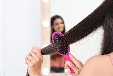 Photo of Beautiful young woman with hair brush looking into mirror in bathroom