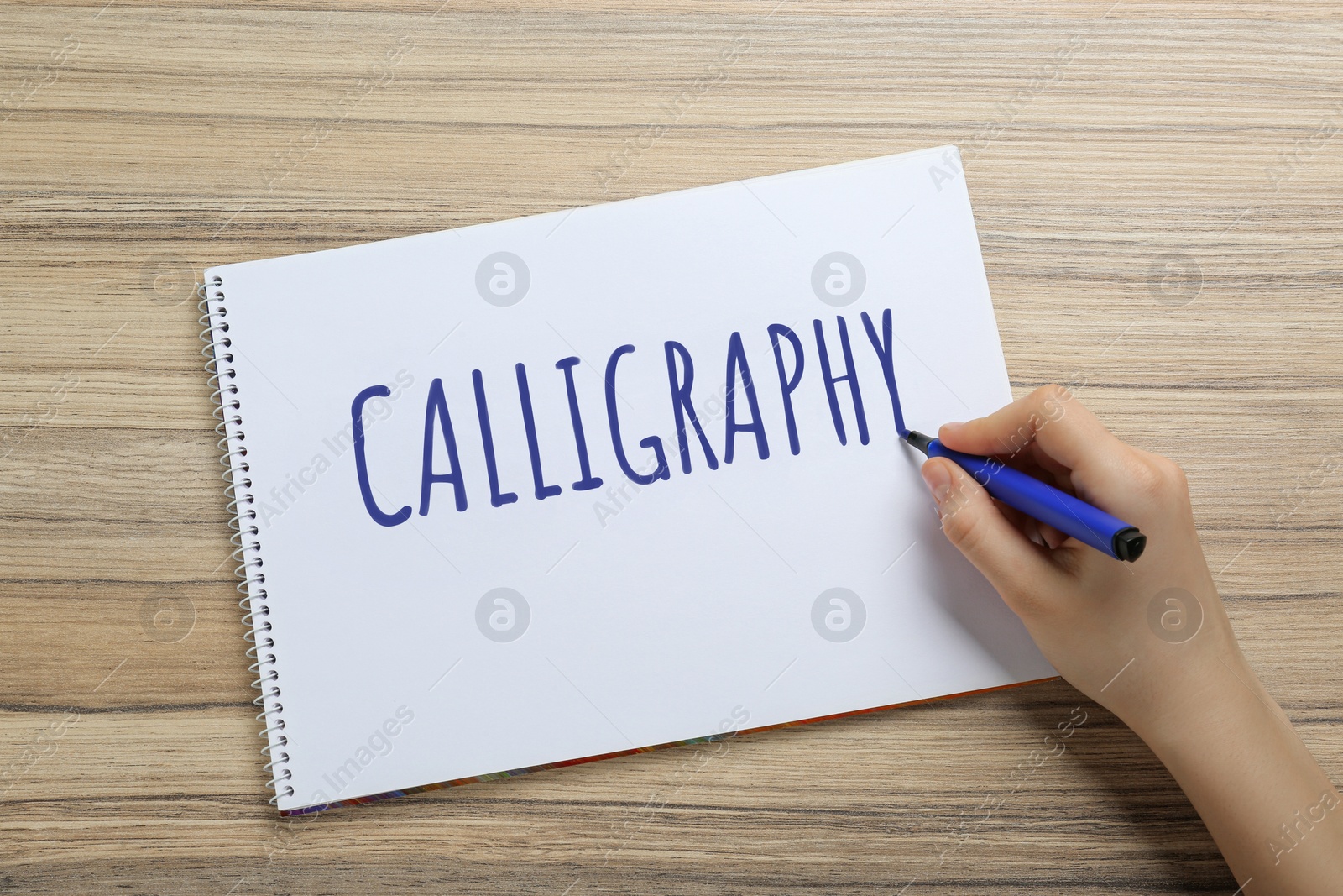 Image of Woman writing word Calligraphy in notebook at wooden table, top view