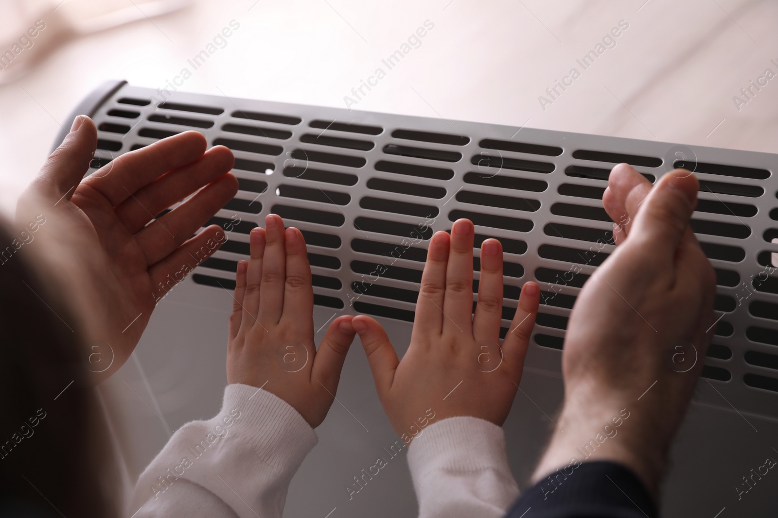 Photo of Father and child warming hands near electric heater at home, closeup