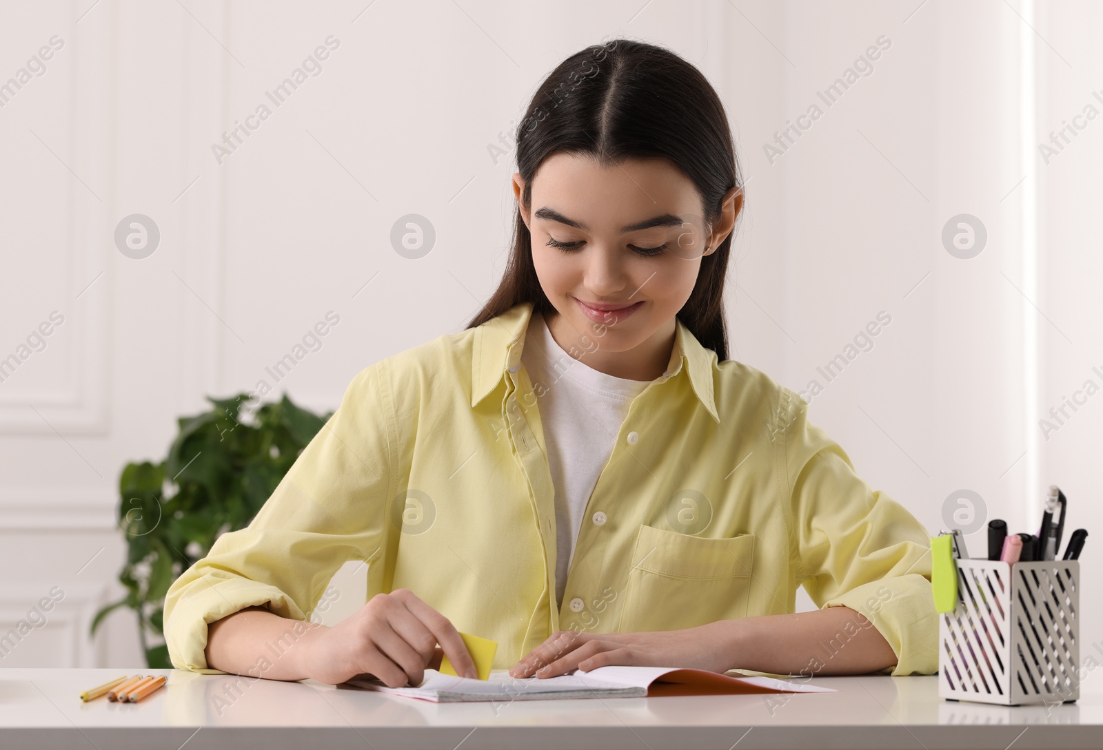 Photo of Teenage girl erasing mistake in her notebook at white desk indoors