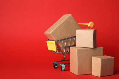 Photo of Shopping cart and boxes on red background, space for text. Logistics and wholesale concept
