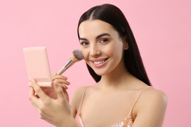 Photo of Beautiful woman with cosmetic pocket mirror applying makeup on pink background