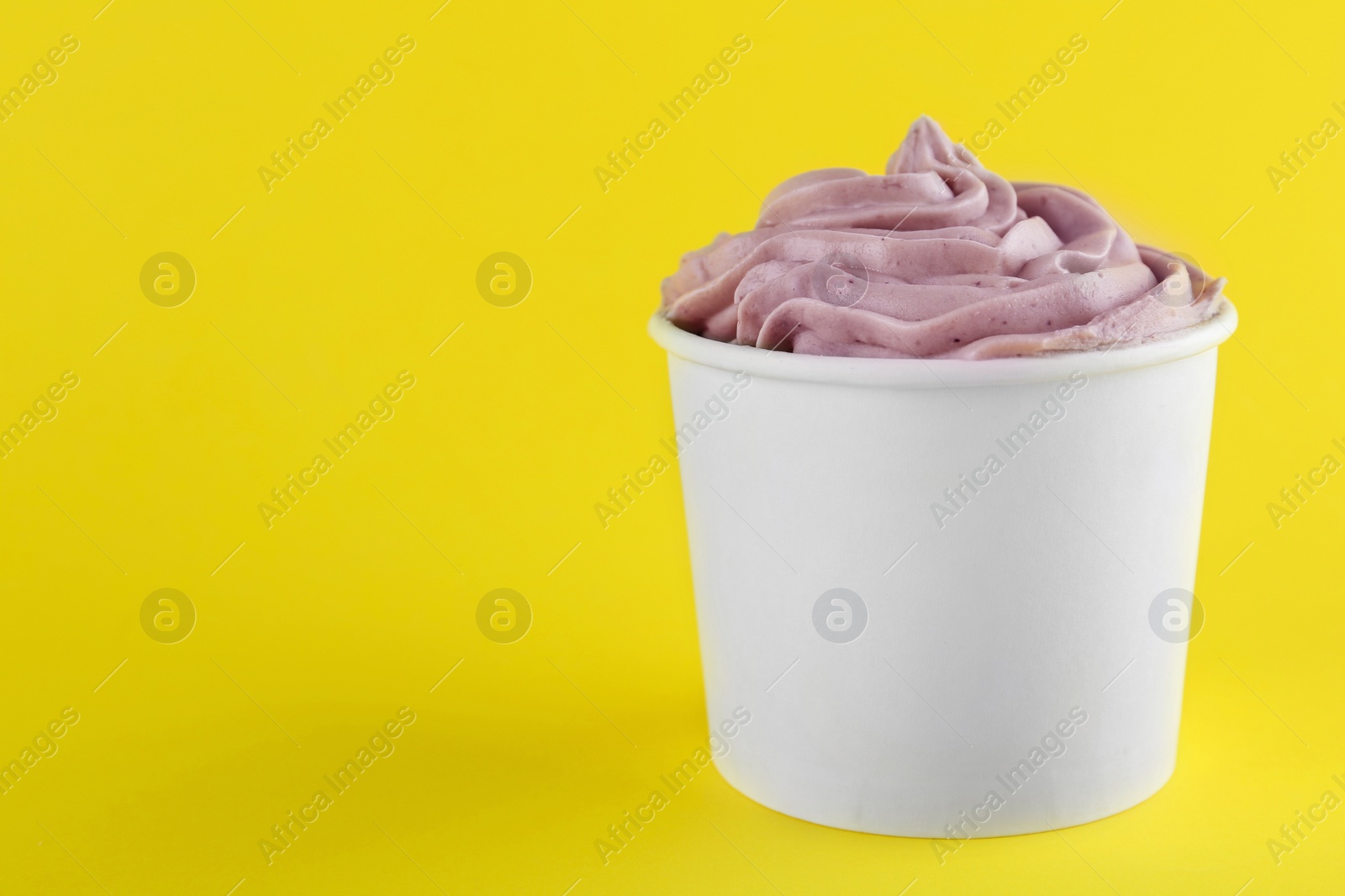 Photo of Cup with tasty frozen yogurt on yellow background. Space for text