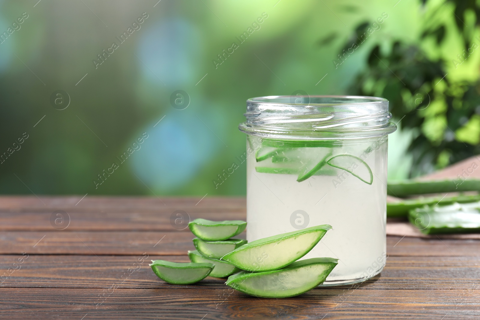 Photo of Fresh aloe juice in jar and cut leaves on wooden table outdoors, space for text