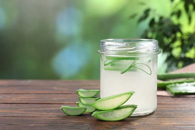 Photo of Fresh aloe juice in jar and cut leaves on wooden table outdoors, space for text