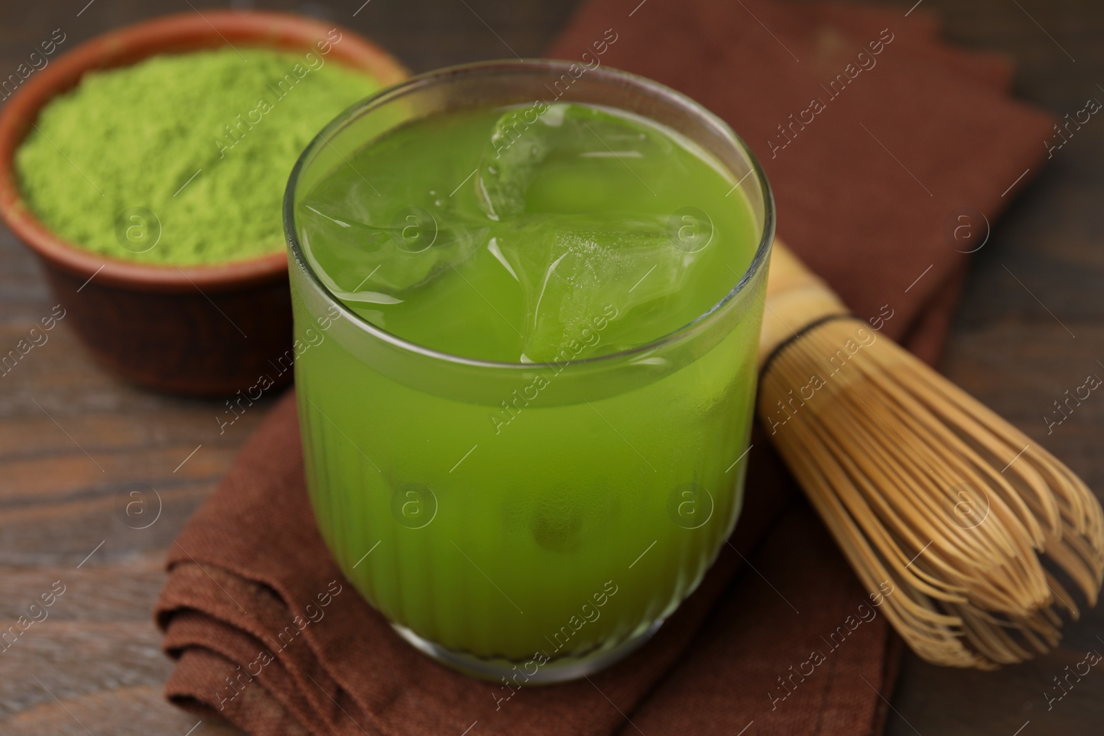 Photo of Glass of delicious iced green matcha tea and bamboo whisk on wooden table, closeup