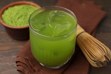 Glass of delicious iced green matcha tea and bamboo whisk on wooden table, closeup