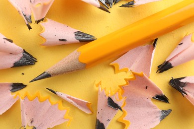 Photo of One sharp graphite pencil and shavings on yellow background, top view