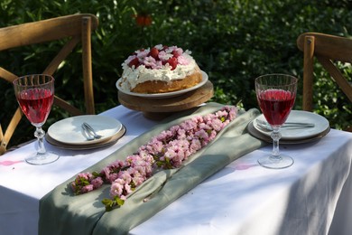 Beautiful spring flowers, delicious cake and wine glasses on table in garden