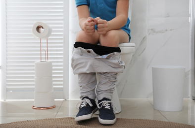 Photo of Boy suffering from hemorrhoid on toilet bowl in rest room, closeup