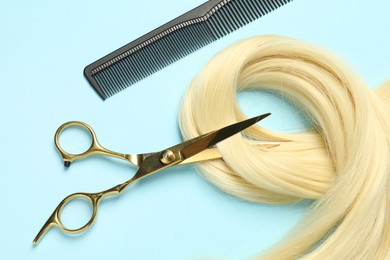 Professional hairdresser scissors and comb with blonde hair strand on light blue background, flat lay
