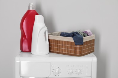 Photo of Baby clothes in wicker basket and laundry detergents on washing machine near light wall