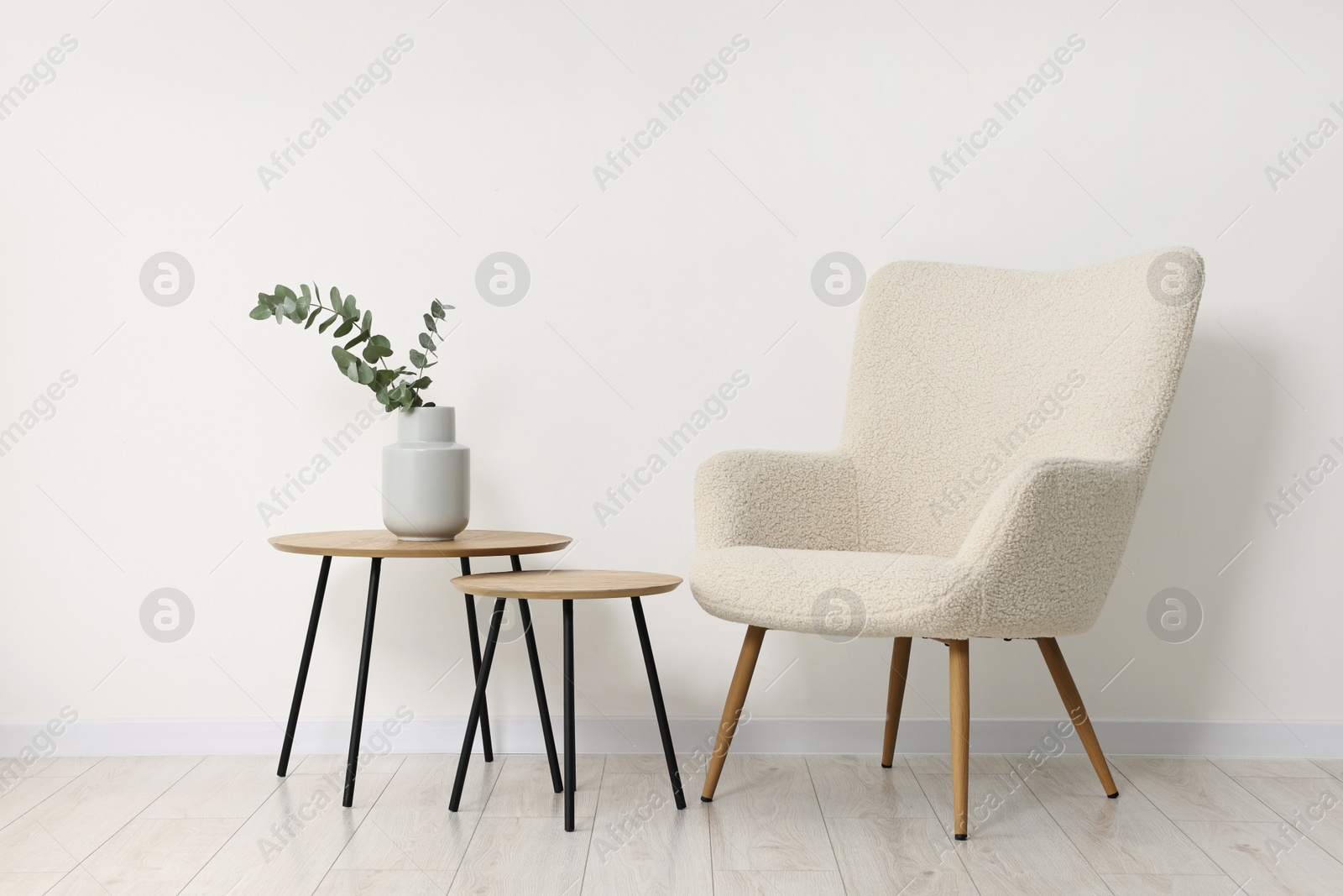 Photo of Comfortable armchair, nesting tables and eucalyptus indoors