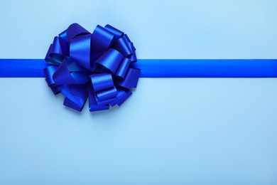 Photo of Ribbon with bow on light blue background, top view. Space for text