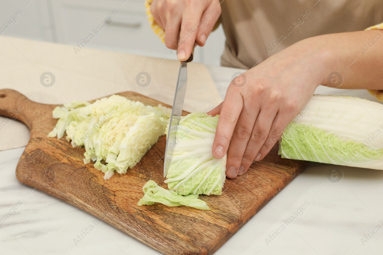 Photo of Woman cutting fresh chinese cabbage at table in kitchen, closeup