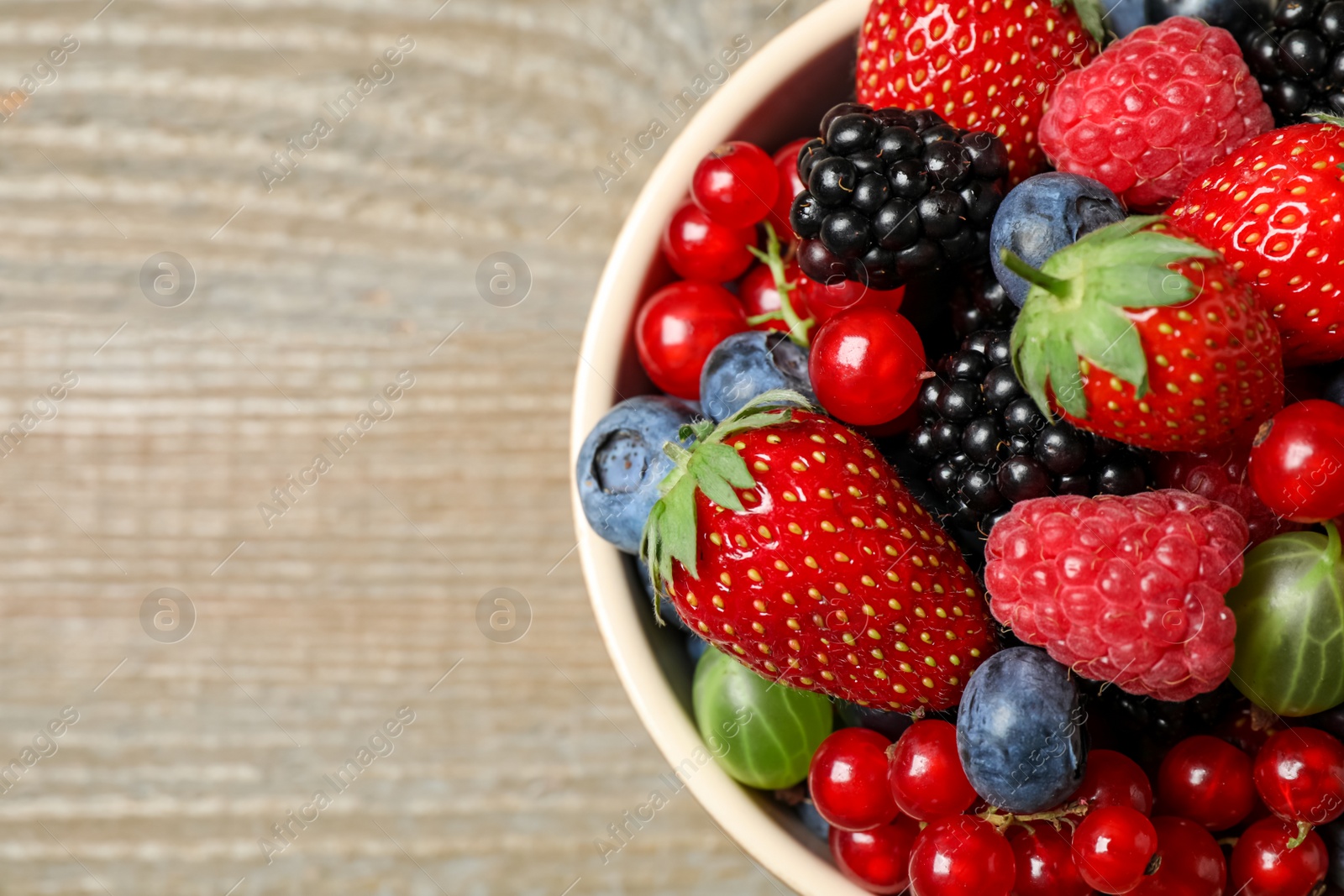 Photo of Mix of different fresh berries in bowl on wooden table, top view. Space for text