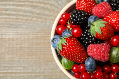 Photo of Mix of different fresh berries in bowl on wooden table, top view. Space for text