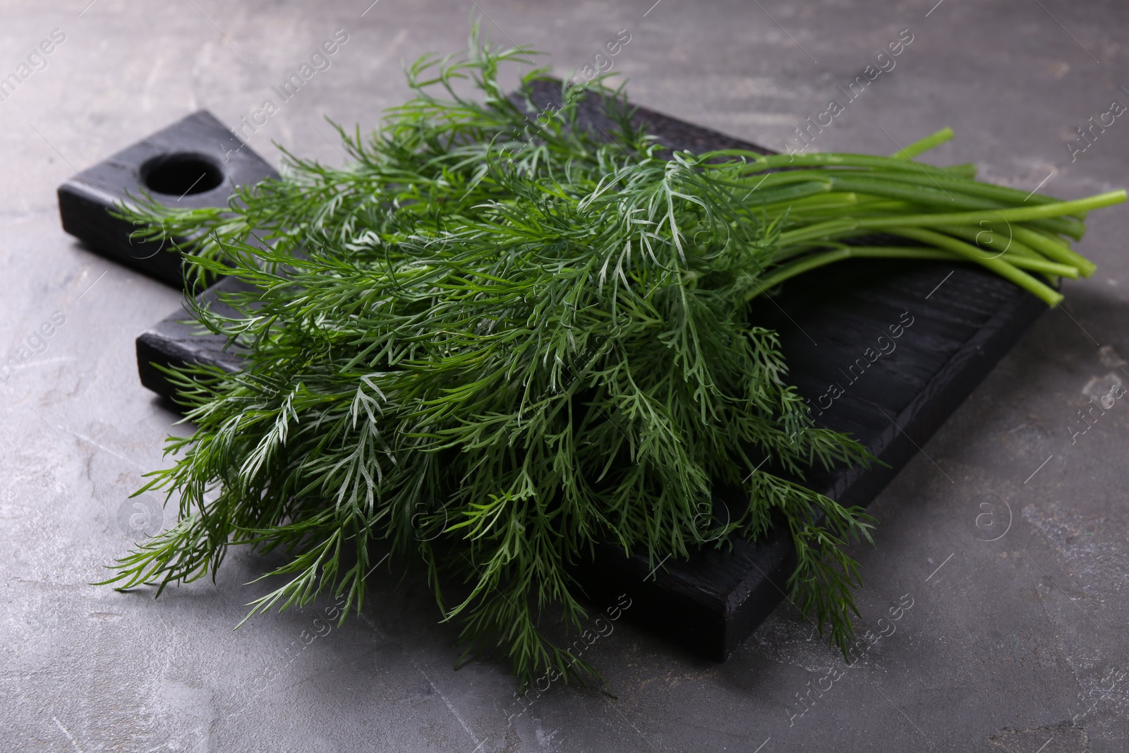 Photo of Board with sprigs of fresh dill on grey textured table, closeup