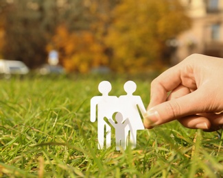 Photo of Woman holding paper silhouette of family in grass outdoors, space for text. Life insurance concept