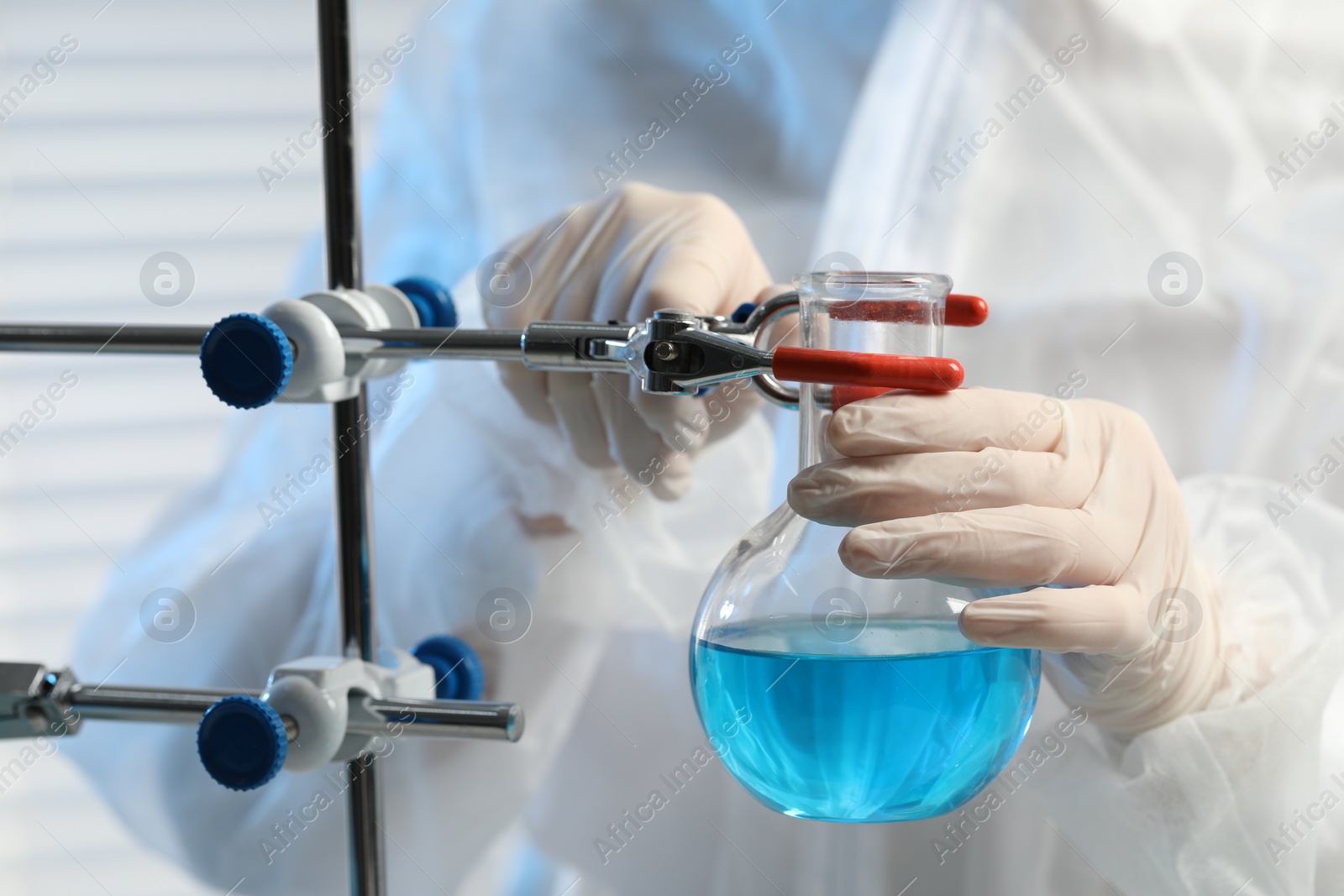 Photo of Scientist working with flask of light blue liquid in laboratory, closeup