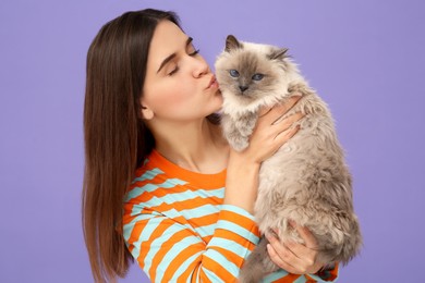 Woman kissing her cute cat on violet background