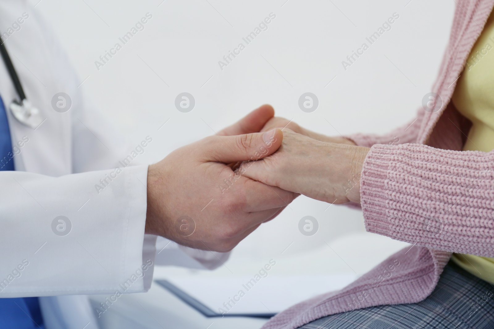 Image of Doctor and senior patient holding hands in hospital, closeup