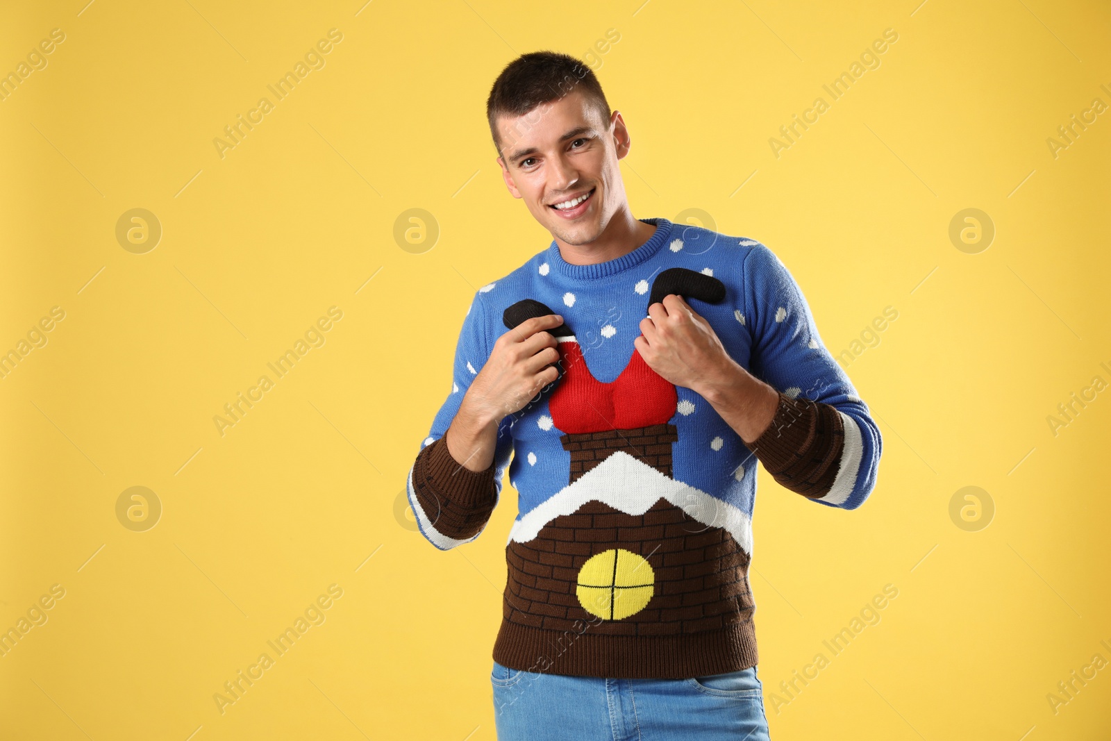 Photo of Portrait of happy young man in Christmas sweater on yellow background