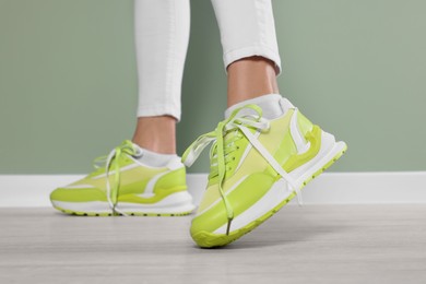 Photo of Woman wearing pair of new stylish sneakers near light green wall, closeup