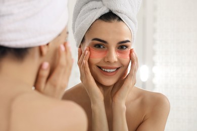 Beautiful young woman with under eye patches near mirror at home