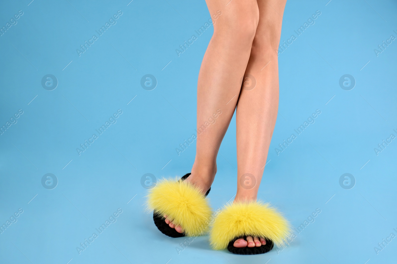 Photo of Woman in fluffy slippers on light blue background, closeup