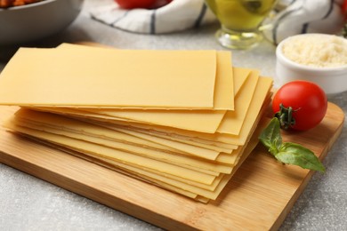 Photo of Cooking lasagna. Wooden board with pasta sheets and tomato on grey textured table, closeup