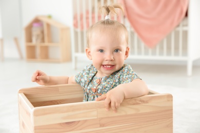 Adorable baby girl playing in wooden cart at home