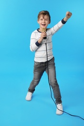 Cute boy singing in microphone on color background